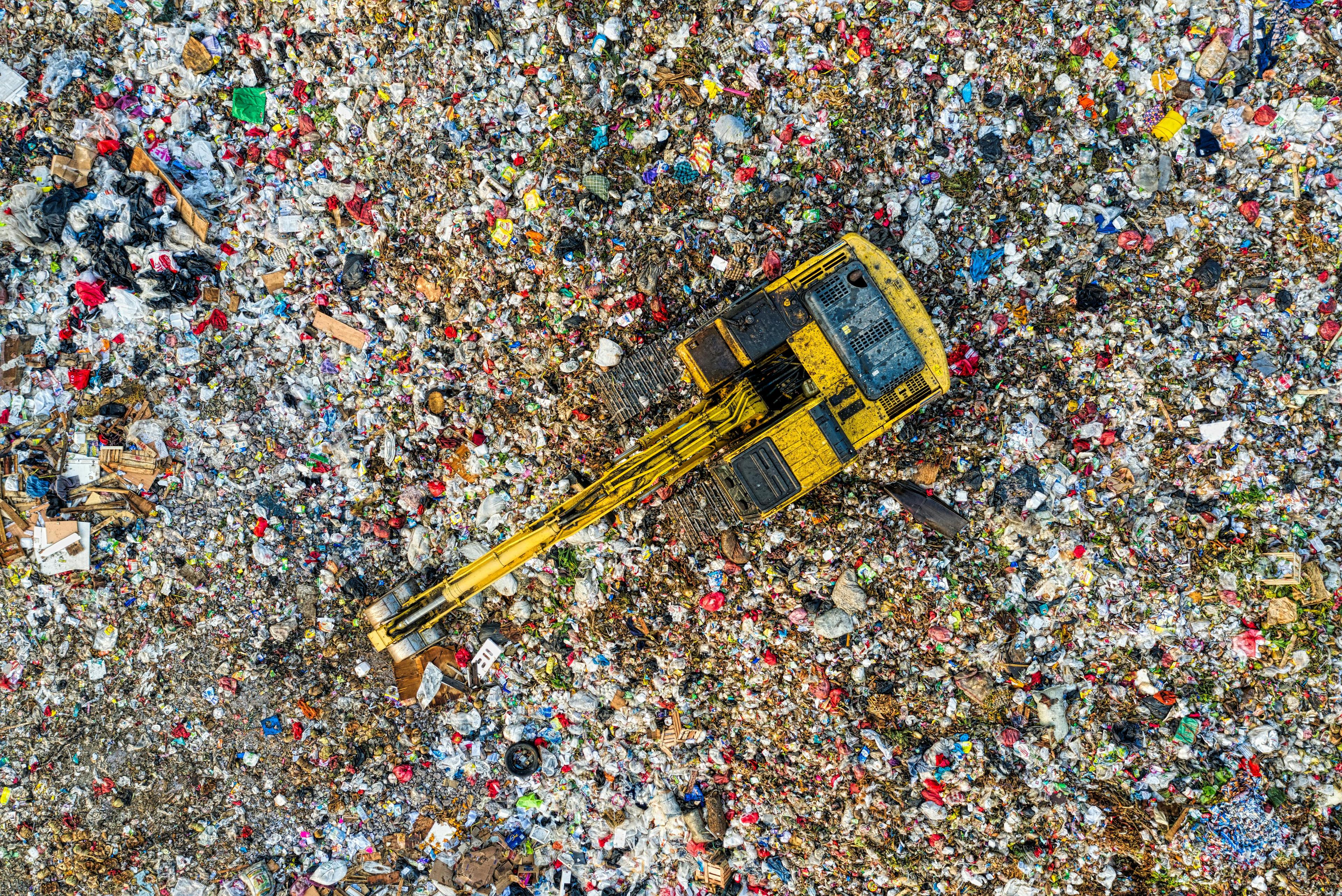 An excavator working across a landfill from above.