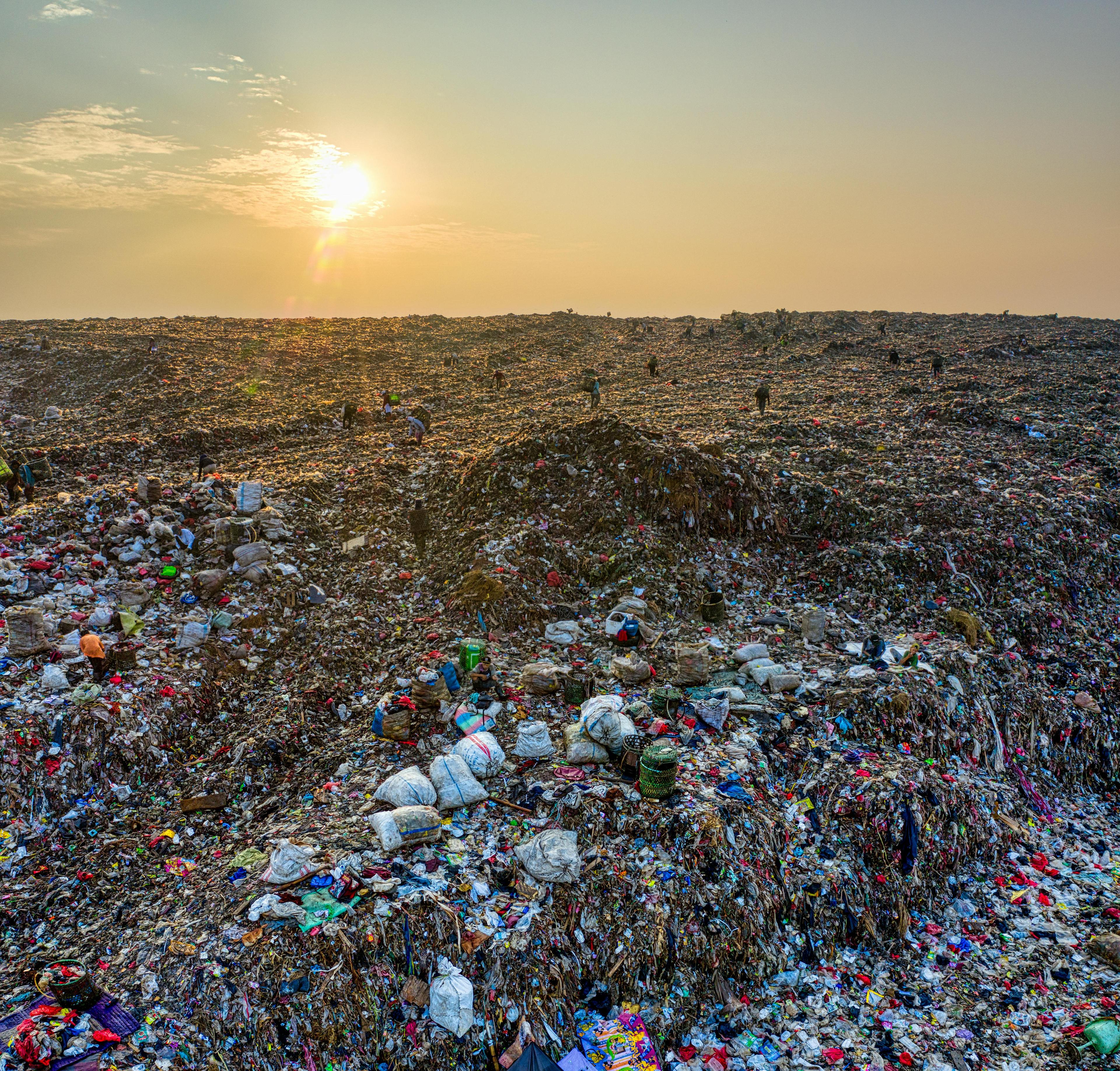 A landfill horizon filled with plastic waste at sunset.